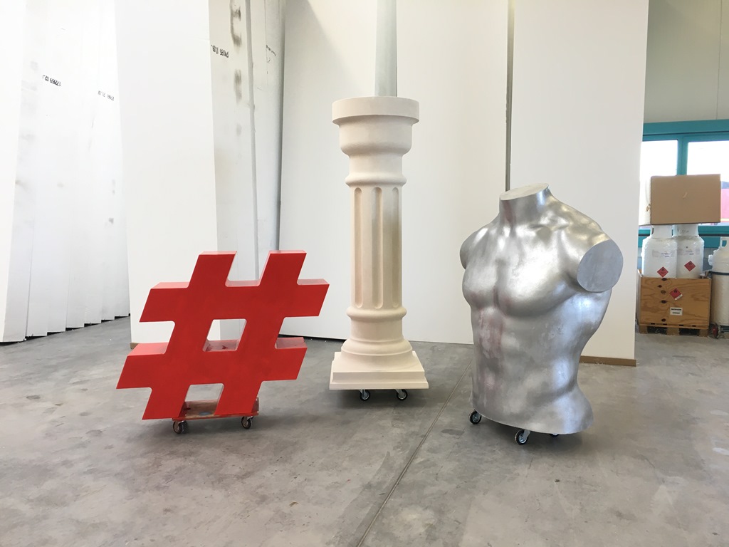 Dekorative Ausstellungsobjekte aus Styropor – rotes Hashtag-Symbol, weiße Säule und silberner Männer-Torso auf Rollen